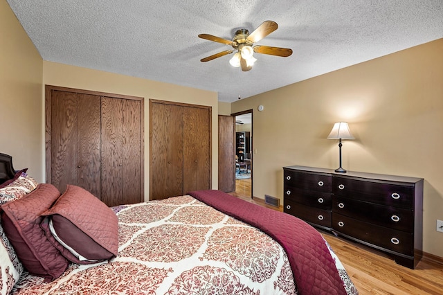 bedroom with ceiling fan, a textured ceiling, light wood-type flooring, and two closets