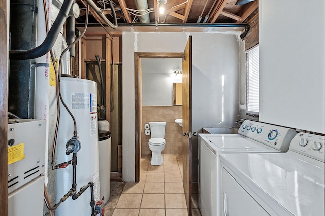 laundry area with light tile patterned flooring, separate washer and dryer, gas water heater, and tile walls