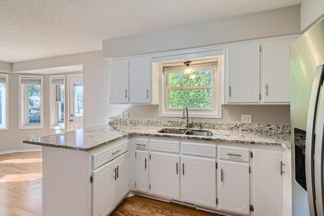 kitchen featuring kitchen peninsula, stainless steel fridge with ice dispenser, white cabinets, and sink