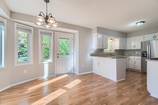 kitchen with stainless steel fridge, light stone counters, kitchen peninsula, and a wealth of natural light