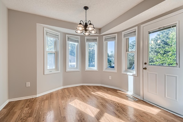 unfurnished dining area featuring light hardwood / wood-style flooring, a chandelier, and a textured ceiling