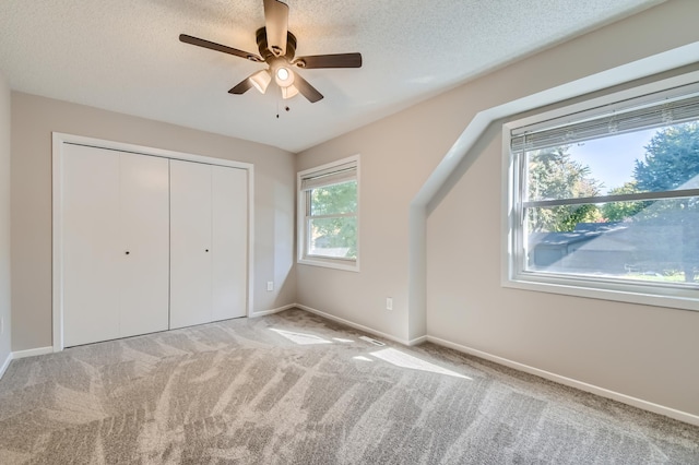 unfurnished bedroom featuring light carpet, a textured ceiling, a closet, and ceiling fan