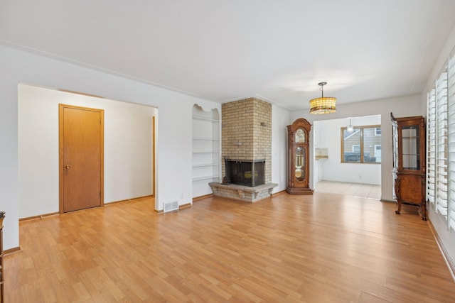 unfurnished living room with built in features, light wood-type flooring, a brick fireplace, and ornamental molding