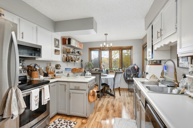 kitchen featuring stainless steel appliances, a textured ceiling, sink, light hardwood / wood-style flooring, and decorative light fixtures