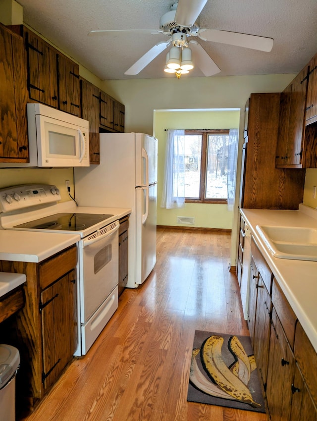 kitchen with white appliances, light wood-type flooring, ceiling fan, a textured ceiling, and sink