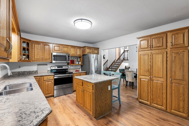 kitchen with sink, light hardwood / wood-style flooring, a textured ceiling, a kitchen island, and appliances with stainless steel finishes