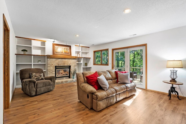 living room featuring a textured ceiling, light wood-type flooring, and a stone fireplace