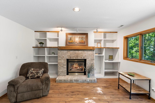 living room featuring a fireplace, rail lighting, wood-type flooring, and a textured ceiling