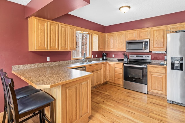 kitchen with light hardwood / wood-style floors, kitchen peninsula, sink, a breakfast bar area, and appliances with stainless steel finishes