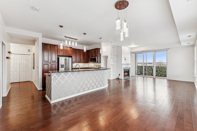 kitchen featuring appliances with stainless steel finishes, dark hardwood / wood-style flooring, sink, pendant lighting, and an island with sink