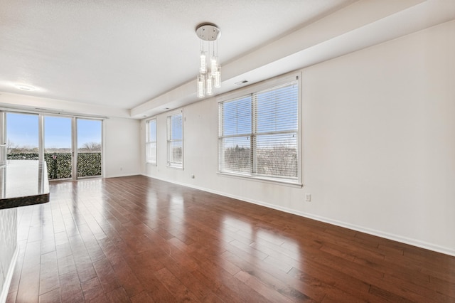 unfurnished living room with dark hardwood / wood-style flooring, a tray ceiling, a wealth of natural light, and a notable chandelier