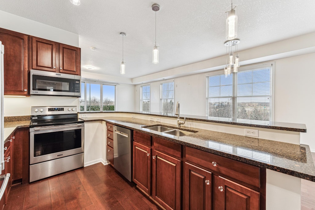 kitchen with kitchen peninsula, appliances with stainless steel finishes, dark stone counters, sink, and hanging light fixtures