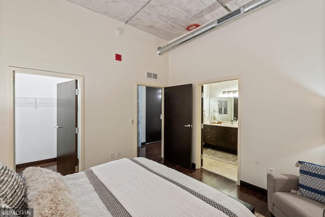 bedroom featuring dark wood-type flooring, ensuite bathroom, a high ceiling, a spacious closet, and a closet