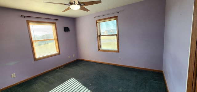 empty room with a wealth of natural light, ceiling fan, and dark colored carpet