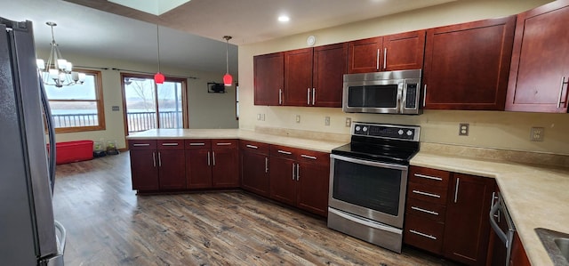 kitchen featuring dark hardwood / wood-style floors, appliances with stainless steel finishes, decorative light fixtures, kitchen peninsula, and a chandelier