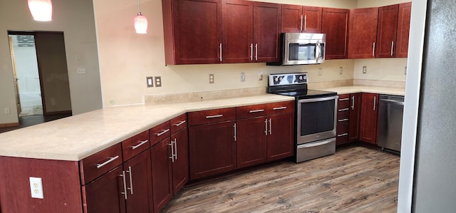 kitchen with kitchen peninsula, appliances with stainless steel finishes, decorative light fixtures, and wood-type flooring