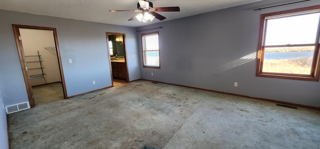 unfurnished bedroom featuring ensuite bathroom, light colored carpet, ceiling fan, a spacious closet, and a closet