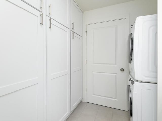 laundry area featuring cabinets, light tile patterned floors, and stacked washer and clothes dryer