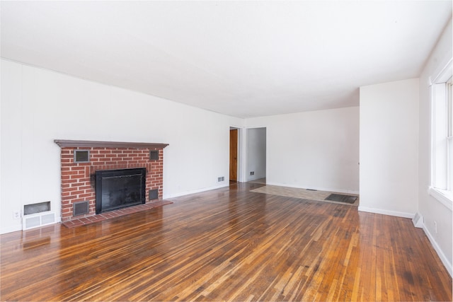 unfurnished living room with a brick fireplace and dark wood-type flooring