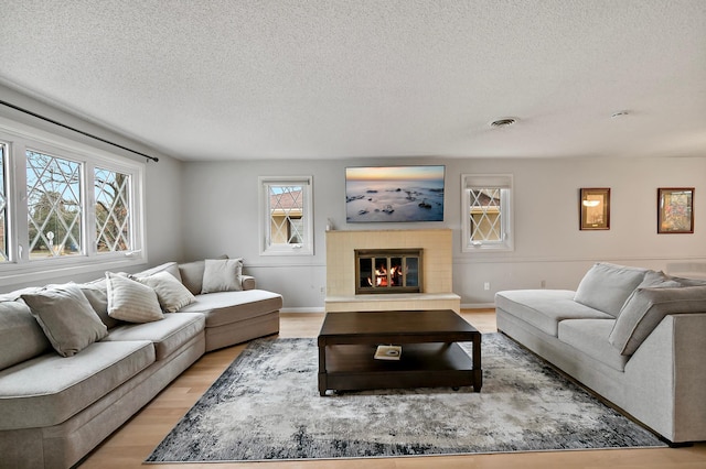 living room featuring light hardwood / wood-style floors, a textured ceiling, and a tile fireplace