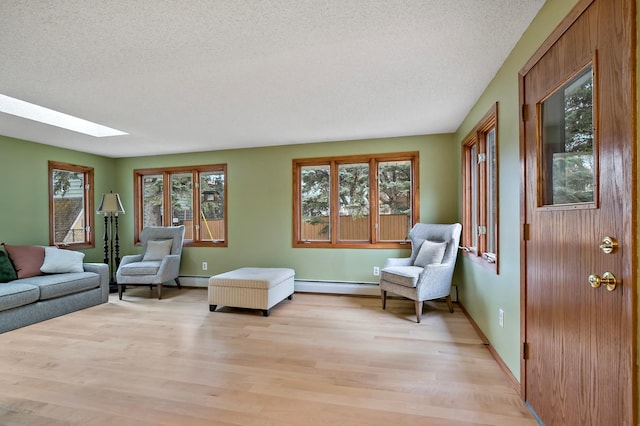 living room featuring a skylight, light hardwood / wood-style floors, a textured ceiling, and a baseboard heating unit