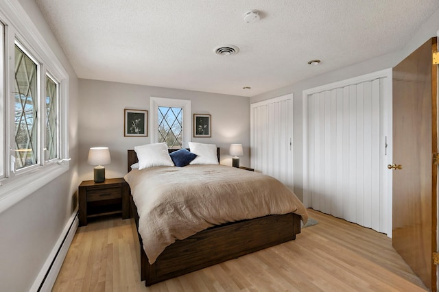 bedroom featuring a textured ceiling, light hardwood / wood-style floors, a baseboard radiator, and multiple windows