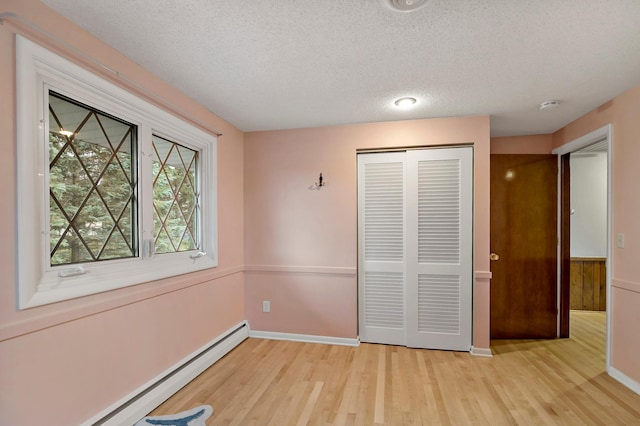 unfurnished bedroom featuring a closet, light wood-type flooring, a textured ceiling, and a baseboard radiator