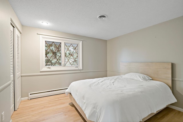 bedroom with a textured ceiling, light wood-type flooring, a baseboard radiator, and a closet