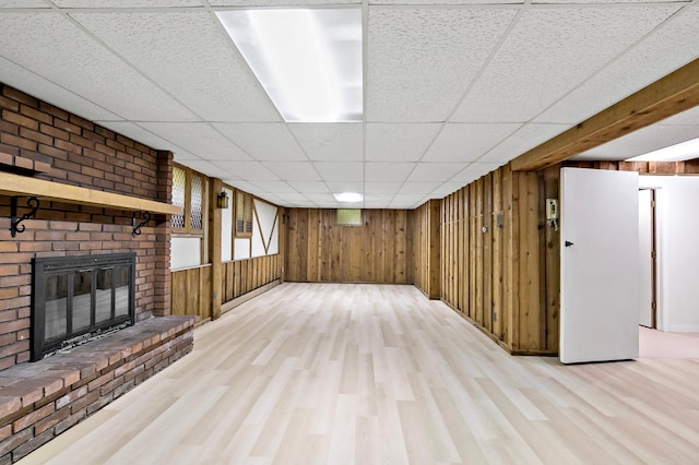 interior space with wood walls, a drop ceiling, light hardwood / wood-style floors, and a brick fireplace