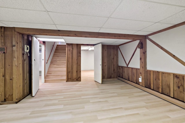 basement with wood walls, a drop ceiling, a baseboard heating unit, and light wood-type flooring