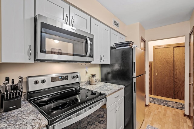 kitchen featuring white cabinetry, light wood-type flooring, appliances with stainless steel finishes, and light stone counters