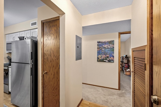 corridor with electric panel, light hardwood / wood-style floors, and a textured ceiling