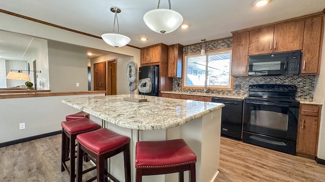 kitchen with light wood-type flooring, a center island, a breakfast bar area, and black appliances