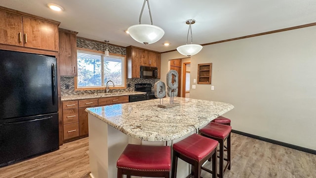 kitchen with sink, crown molding, a kitchen island, black appliances, and light wood-type flooring