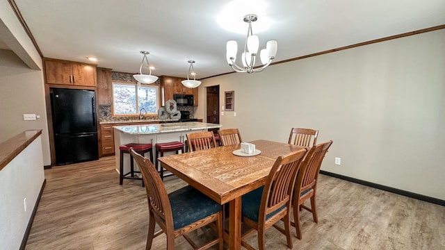 dining space featuring a notable chandelier, light wood-type flooring, sink, and ornamental molding