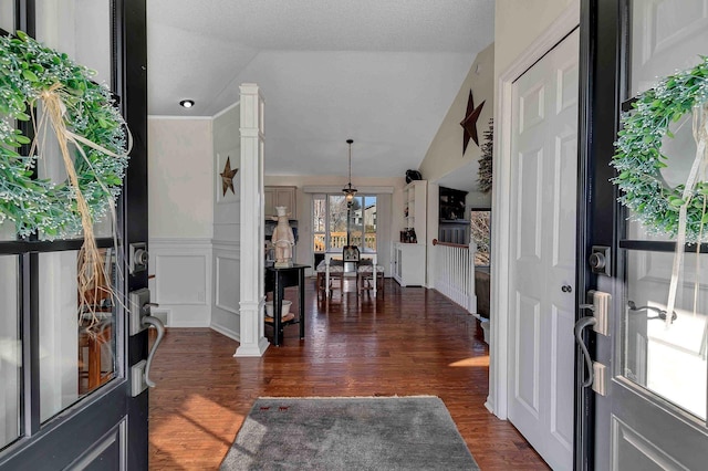 entrance foyer with dark wood-type flooring, a textured ceiling, ornate columns, and vaulted ceiling