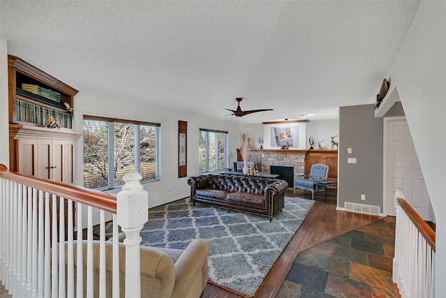 living room with dark wood-type flooring, a fireplace, a textured ceiling, and ceiling fan