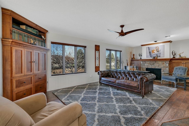 living room with ceiling fan, dark hardwood / wood-style floors, a textured ceiling, and a stone fireplace