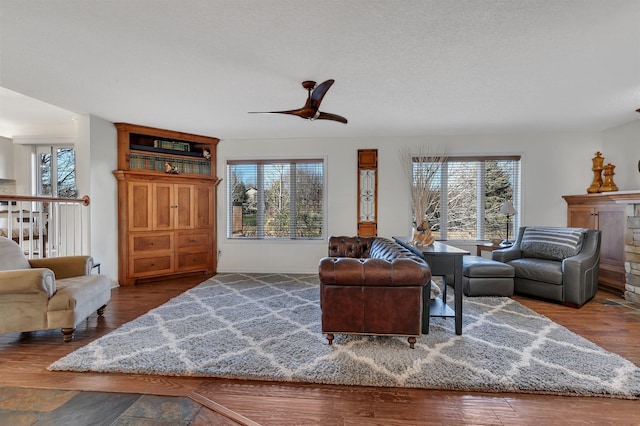 living room with a textured ceiling, hardwood / wood-style floors, ceiling fan, and a fireplace