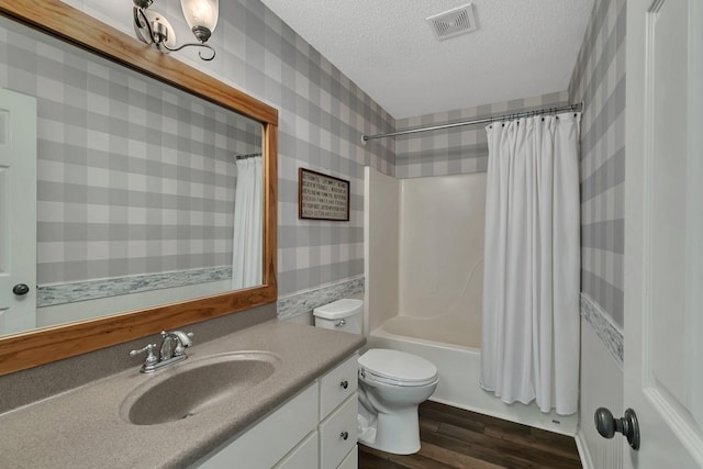 full bathroom with toilet, a textured ceiling, hardwood / wood-style flooring, vanity, and shower / tub combo