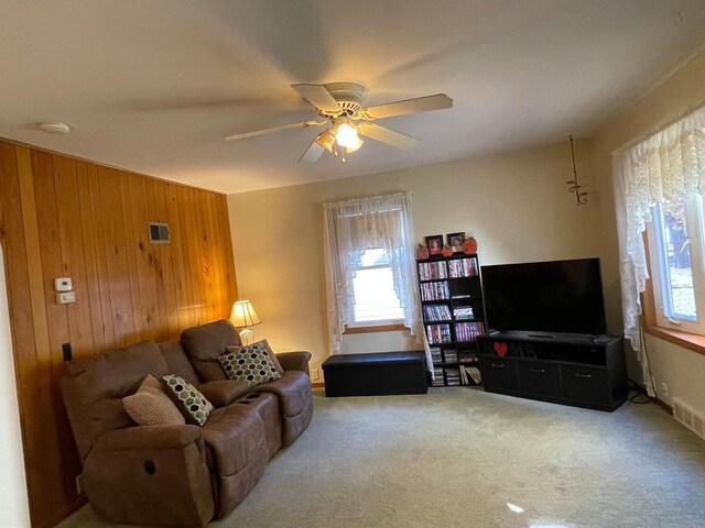 living room with ceiling fan, wooden walls, and carpet