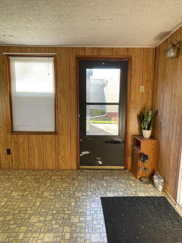 doorway to outside with a textured ceiling and wooden walls