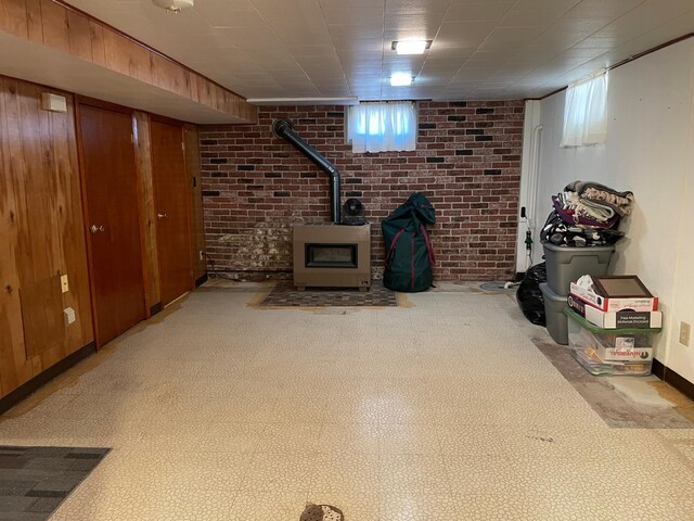 basement featuring light carpet, a wood stove, plenty of natural light, and brick wall