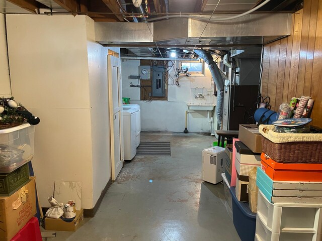 basement with electric panel, wood walls, washer and clothes dryer, and heating unit