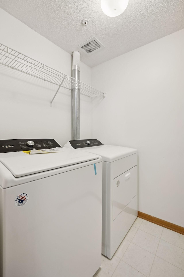 washroom featuring light tile patterned flooring, washer and clothes dryer, and a textured ceiling