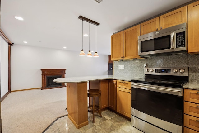 kitchen with pendant lighting, appliances with stainless steel finishes, a kitchen bar, decorative backsplash, and kitchen peninsula