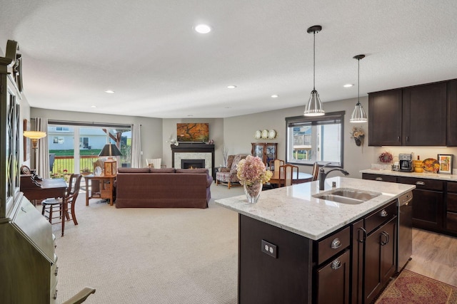 kitchen with light stone countertops, sink, pendant lighting, a center island with sink, and dishwasher