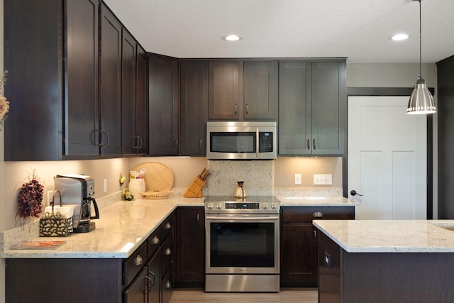 kitchen with light stone countertops, hanging light fixtures, stainless steel appliances, and dark brown cabinets