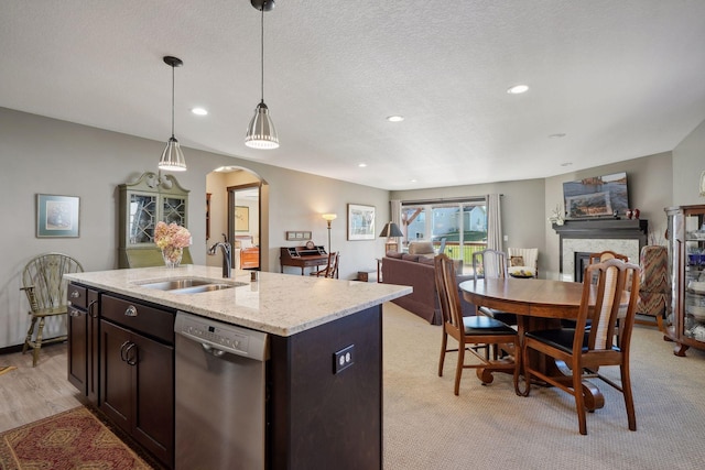 kitchen with sink, light stone counters, stainless steel dishwasher, decorative light fixtures, and a kitchen island with sink