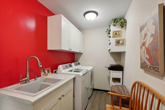 clothes washing area featuring cabinets, a textured ceiling, sink, separate washer and dryer, and light hardwood / wood-style floors